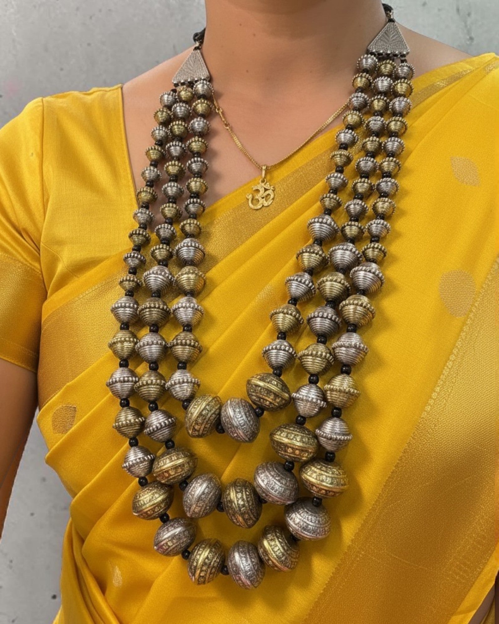 Model wearing the Kanak Layered Bead Mala with dual-tone oxidised engraved beads, styled with a yellow saree for a traditional ethnic look.
