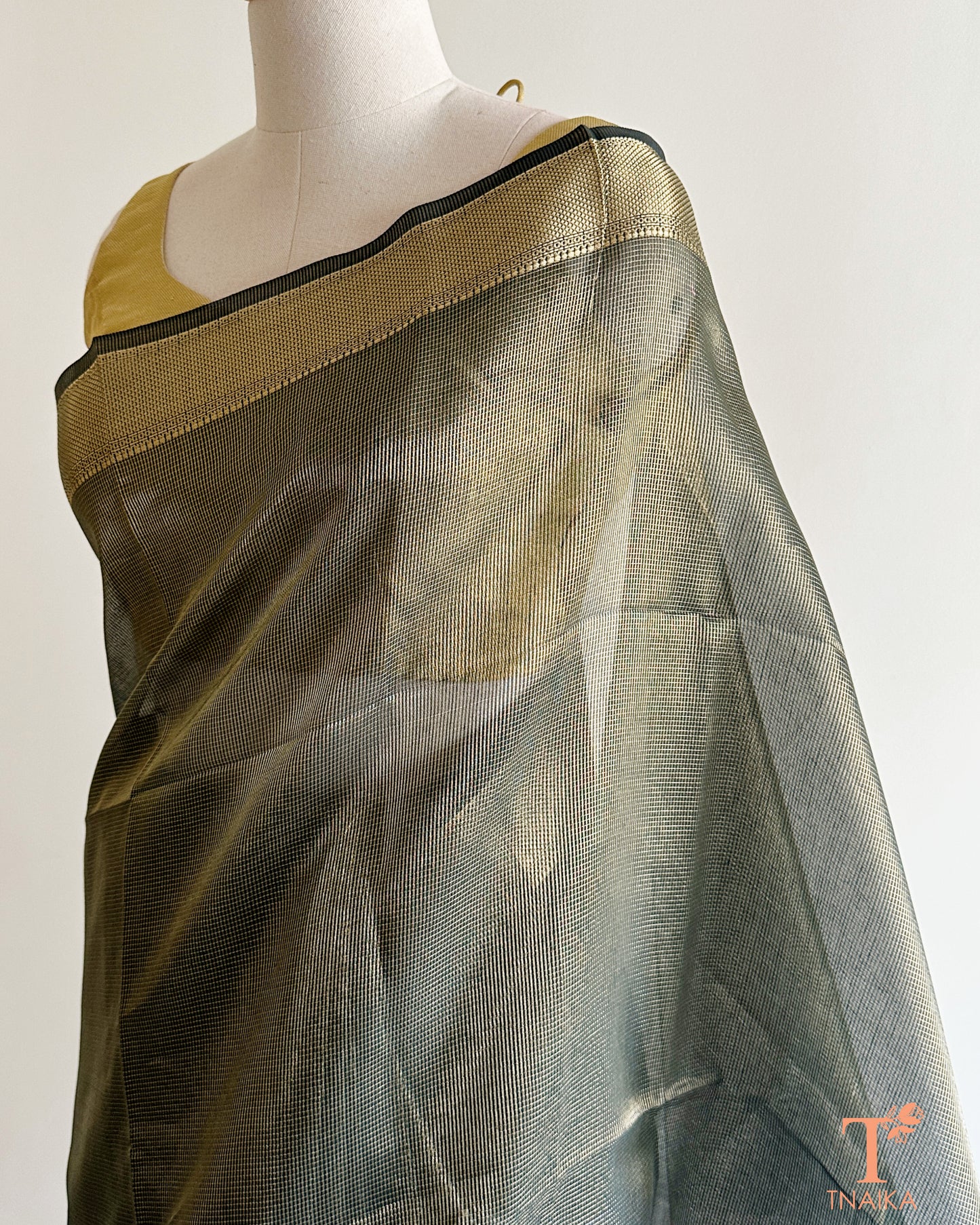 Close-up of muted olive green tissue silk saree featuring fine micro checks, antique gold zari weave, and striped pallu design