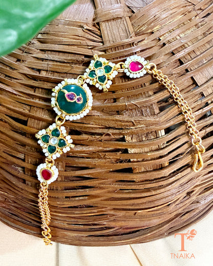 Ethnic brass bracelet with green enamel centerpiece and ruby-toned kundan accents.