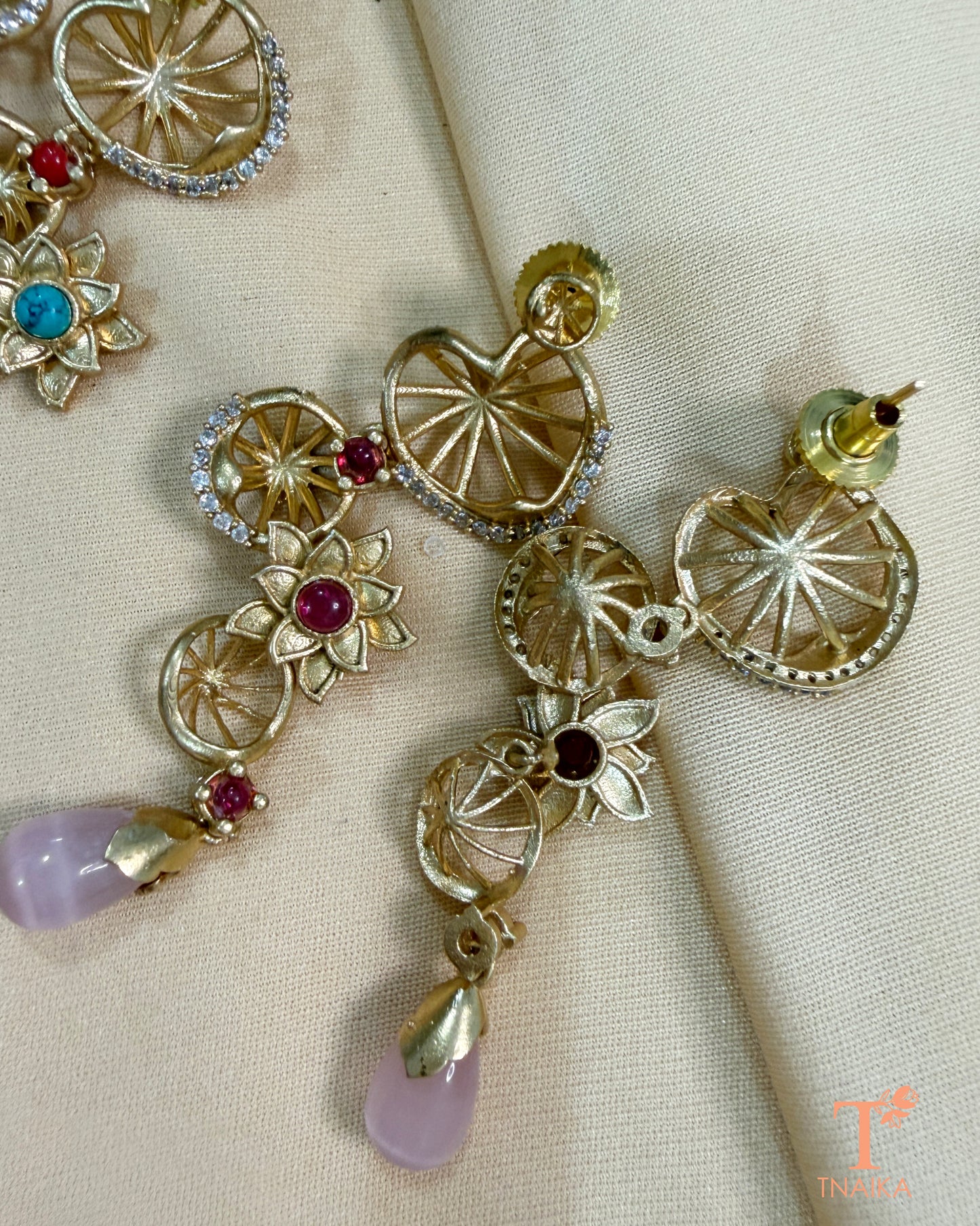 Elegant floral statement earrings with ruby-toned centre stones, gold finish and soft pink hanging drops for festive wear.