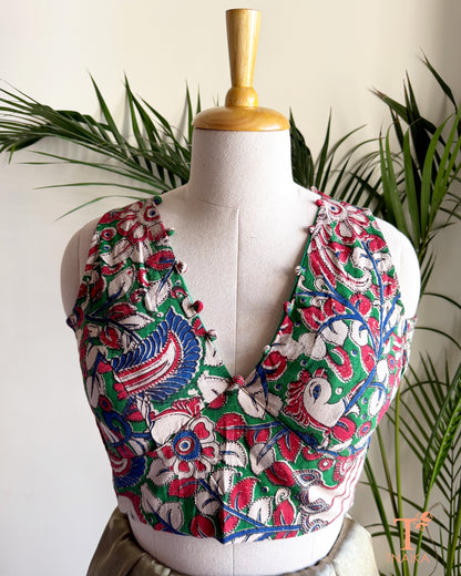 Tnaika™ handcrafted Kalamkari cotton blouse with a flattering V-neckline, fabric potli detailing, and vibrant floral and peacock-inspired print.