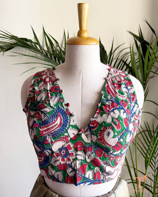 Tnaika™ handcrafted Kalamkari cotton blouse with a flattering V-neckline, fabric potli detailing, and vibrant floral and peacock-inspired print.