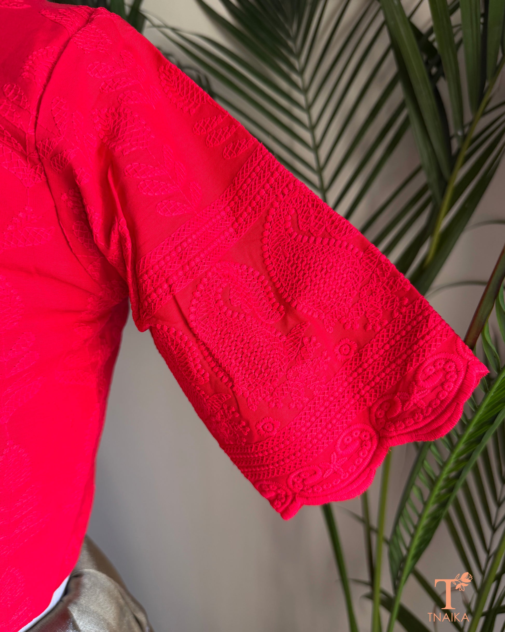Side profile of red cotton blouse showcasing embroidered cutwork sleeve detailing.