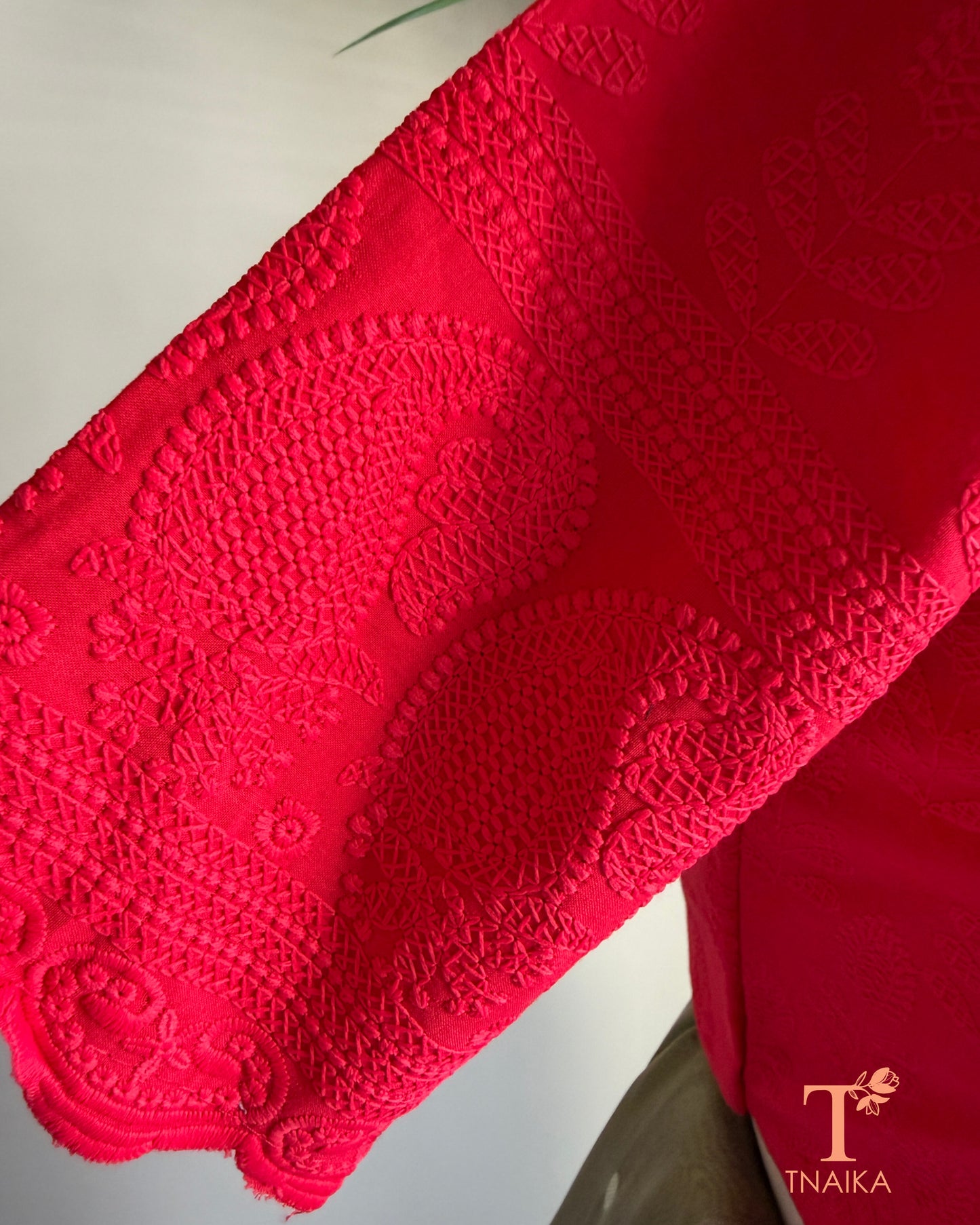 Side profile of red cotton blouse showcasing embroidered cutwork sleeve detailing.