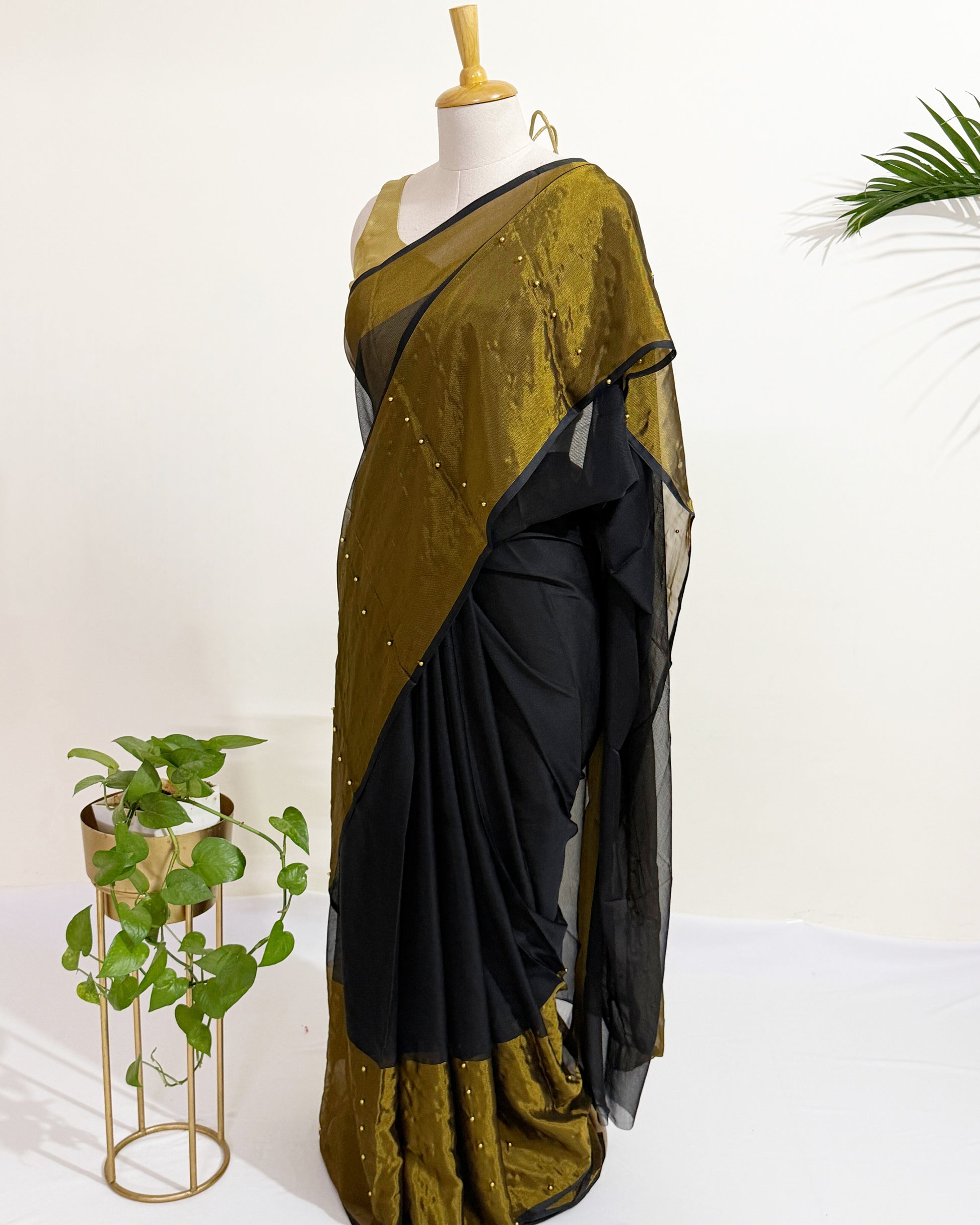 Black chiffon saree with antique gold tissue border and pearl pin embellishments.