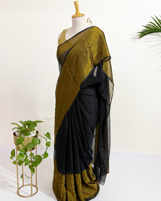 Black chiffon saree with antique gold tissue border and pearl pin embellishments.