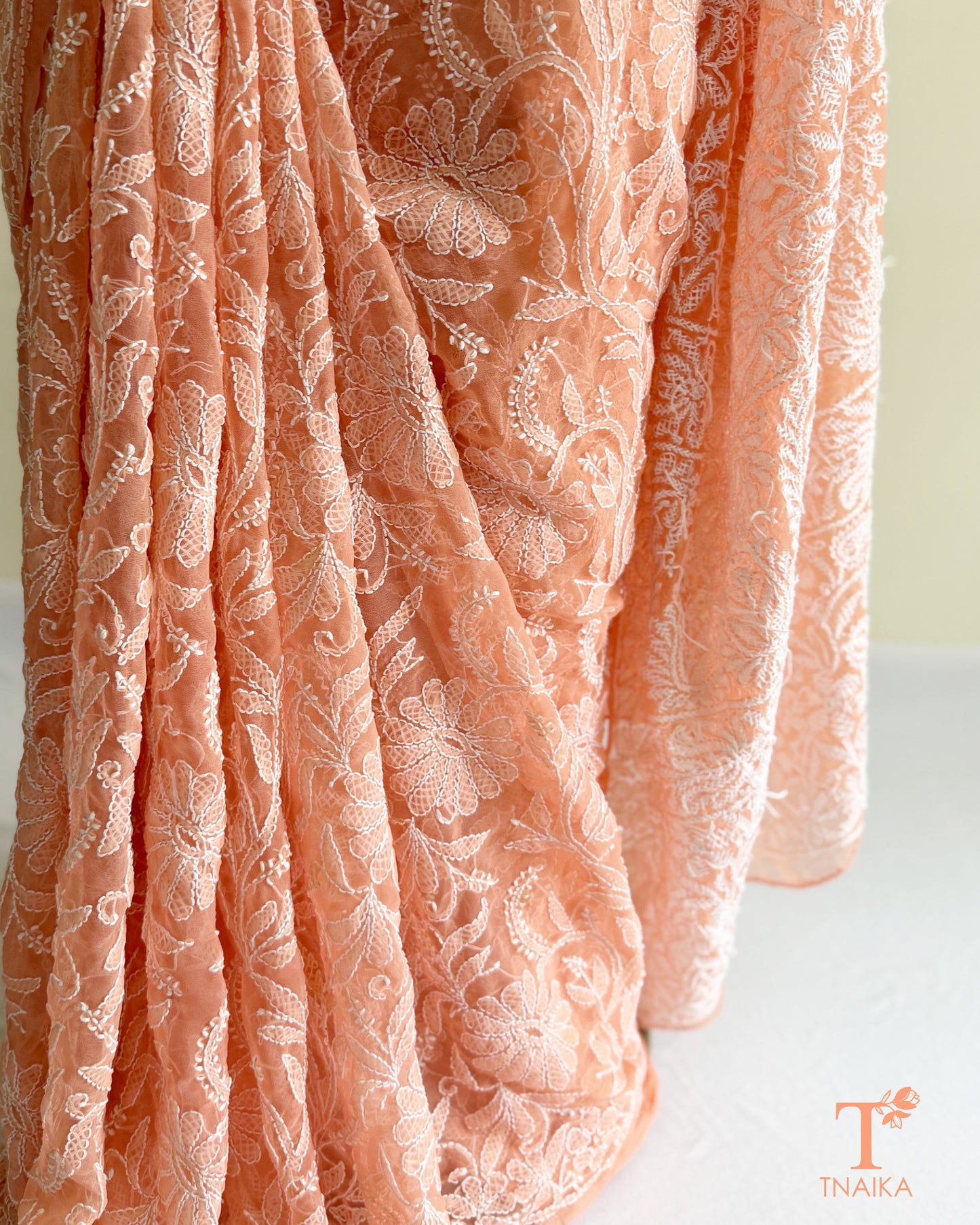 Pastel peach pink Chikankari saree featuring all-over floral embroidery and graceful handcrafted detailing.