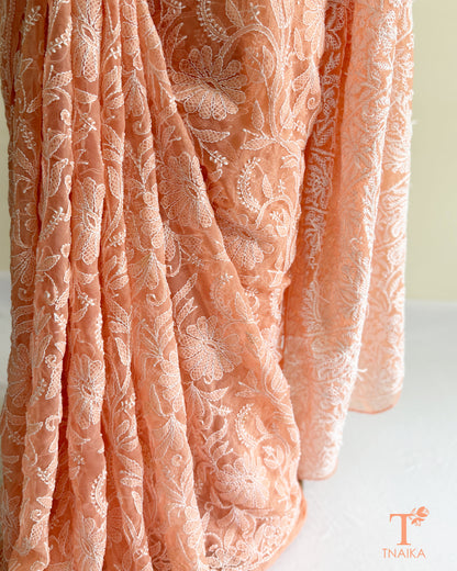 Pastel peach pink Chikankari saree featuring all-over floral embroidery and graceful handcrafted detailing.
