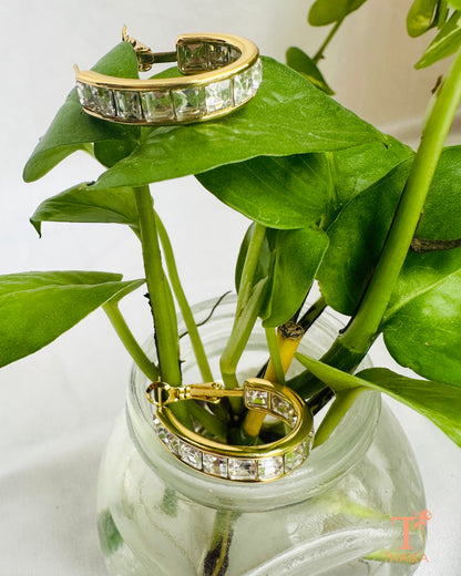 Gold crystal hoop earrings displayed on white fabric