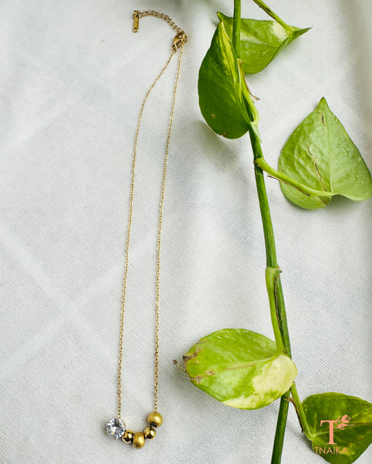 Dainty gold tone necklace featuring a clear crystal and textured bead accents.